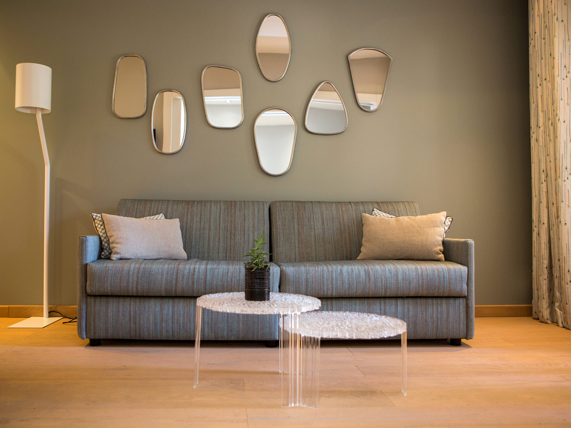 Coin salon moderne d’hôtel avec canapé rayé, miroirs décoratifs et tables basses transparentes