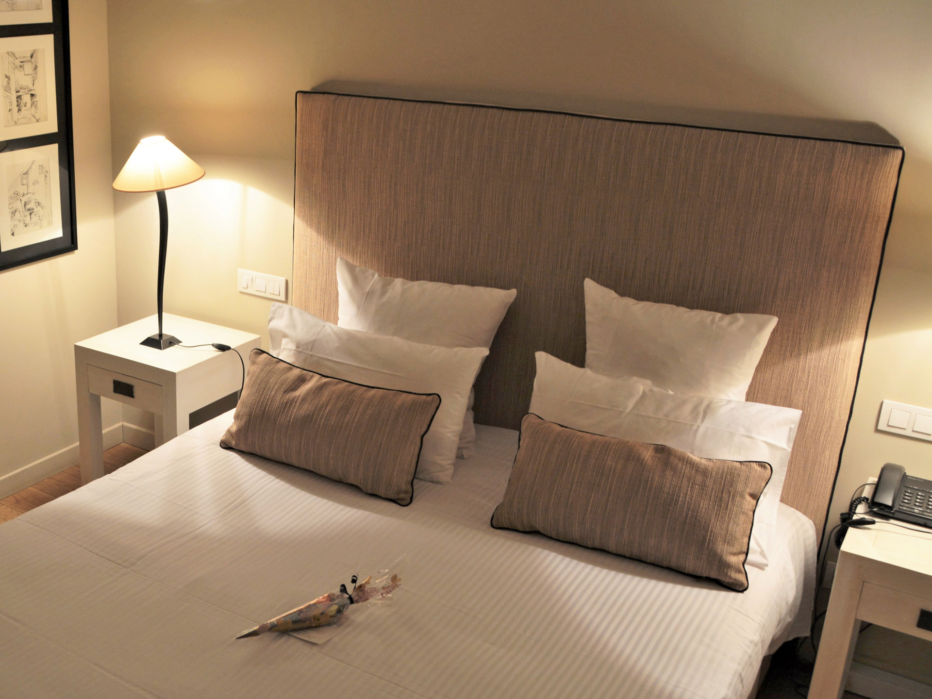 Lit de la suite de l’hôtel avec tête de lit beige et éclairage chaleureux