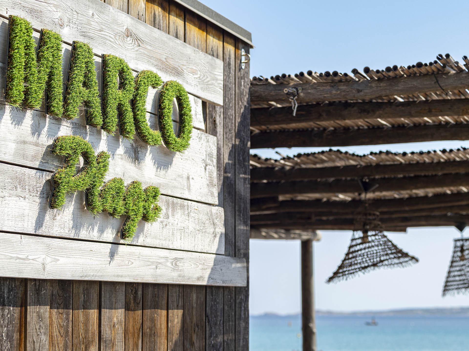 Entrée en bois de Marco Plage avec enseigne végétale et vue sur la mer